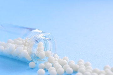 Close up homeopathic globules and glass bottle on blue background. Alternative Homeopathy medicine herbs, healtcare and pills concept. Flatlay. copyspace for text