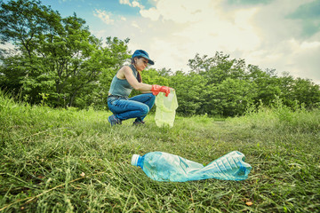 Young  girl picking up the garbage and putting it in a garbage bag on a natural background.