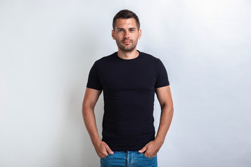 Nice man wearing in black t-shirt standing holding his arms in pocket, seriously looking at the...