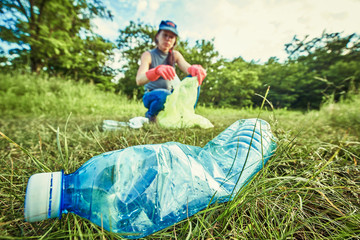 Young  girl picking up the garbage and putting it in a garbage bag on a natural background.