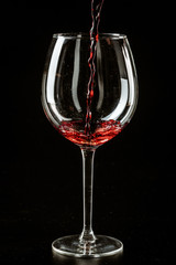 Naklejka na ściany i meble Red wine being poured in a wine glass on a dark background