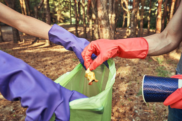 Young  girl picking up the garbage and putting it in a garbage bag on a natural background.