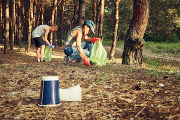 Young  girl picking up the garbage and putting it in a garbage bag on a natural background.