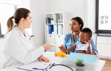 Fototapeta premium medicine, healthcare and pediatry concept - caucasian doctor giving prescription to african american mother with baby son at clinic