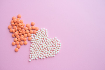 Two hearts made of homeopathic globules and orange pills on pink background. Homeopathy medicine, healtcare, Epidemic, painkillers, drug and pills concept. Flatlay. Top view. copyspace for text