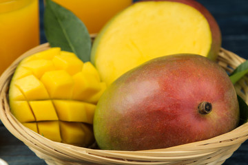 Ripe fresh mango fruit in a basket and slices and leaves on a blue wooden table. tropical fruit.