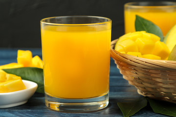 Ripe fresh mango fruit and slices and mango juice in a glass on a blue wooden table. tropical fruit.