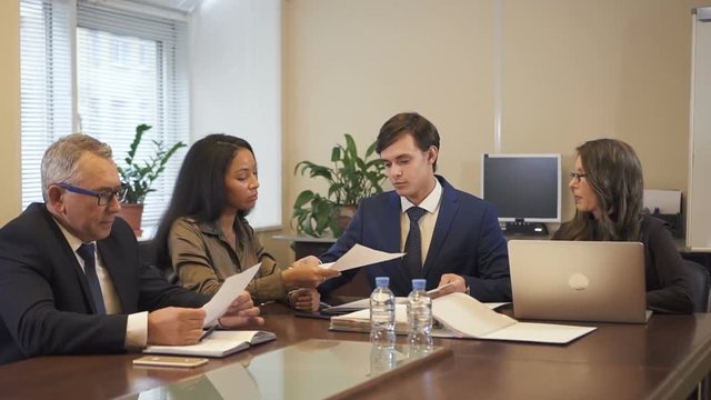 Male solicitor giving contract draft to mature businessman and african-american businesswoman. Senior lawyer sitting near using laptop. Businesspeople making decision.