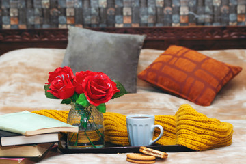 books, chocolate cookies, cup of coffee, roses vase in tray during on bed  the morning