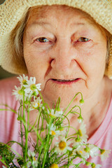 Elderly woman with bouquet of medical daisies in pink T-shirt and hat. Pensioner engaged in...