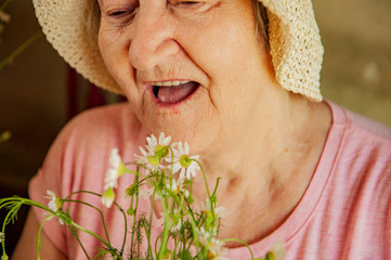 Elderly woman with bouquet of medical daisies in pink T-shirt and hat. Pensioner engaged in...