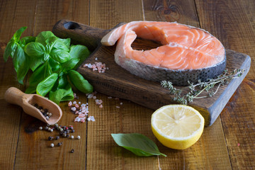 Salmon steak on a chopping Board, thyme, spices, lemon and fresh Basil.