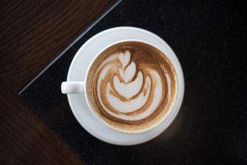 Cup of cappuccino with latte art on black table background. Beautiful foam, place for text.