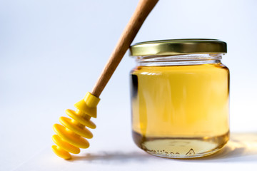 honey in glass jar with wooden dipper on white background