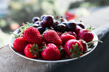 Organic sweet cherry and strawberry on a white plate.