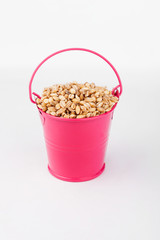 Heap pearl barley grains in pink bucket on white background.