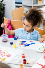 selective focus of african american child holding paintbrush near paper with drawing