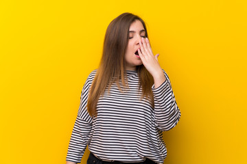Young girl over yellow wall yawning and covering wide open mouth with hand