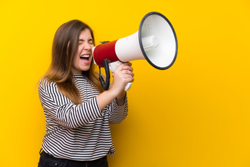 Young girl over yellow wall shouting through a megaphone