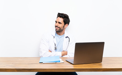 Young doctor man with his laptop over isolated wall looking to the side