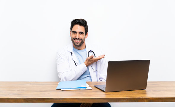 Young doctor man with his laptop over isolated wall extending hands to the side for inviting to come