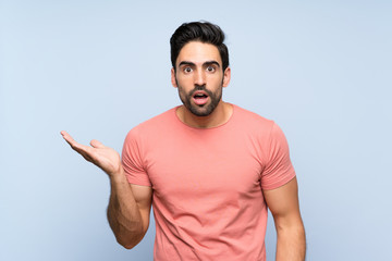 Fototapeta premium Handsome young man in pink shirt over isolated blue background making doubts gesture