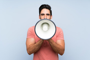 Handsome young man in pink shirt over isolated blue background shouting through a megaphone