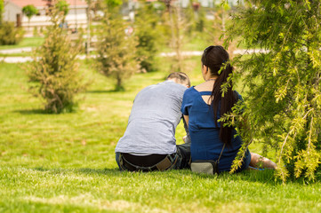 Back side of a young couple sitting on grass in a park on a sunny day