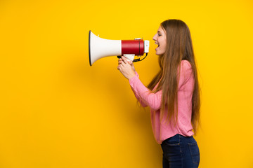 Young woman with long hair over isolated yellow wall shouting through a megaphone