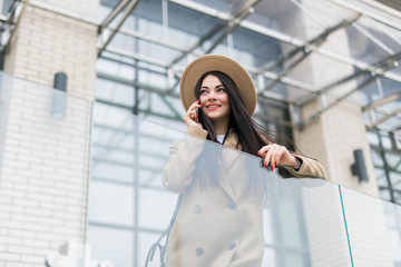 Caucasian business woman speaking by phone. Waist up portrait of a successful European business woman woman, talking on the phone, standing on glass background, modern office building. Sunny weather.