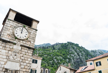Fototapeta na wymiar Clock tower in the Square of the Arms, with the mountains in the background. Kotor, Montenegro. Stone architecture building in old city and green rocks