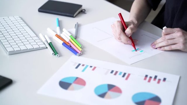 Woman fills data in graphs on paper. Records information. Woman is engaged in office work. Graphic charts,indicators. Woman works at the offside table. Woman draws symbols on the paper