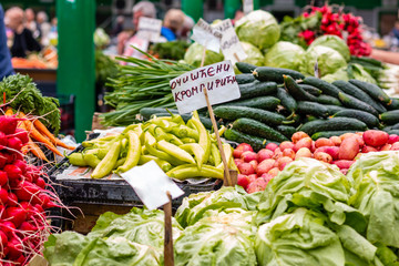 Various fresh vegetables on the marketplace in Belgrade. Blurred sellers and customers on background. Letters "ОЧИШЋЕНИ КРОМПИРИЋИ" means "CLEAN POTATOES"