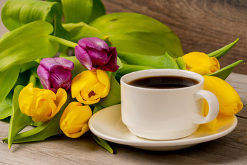 Obraz premium Yellow and purple tulips and coffee cup on rustic wooden table. Close up shot.