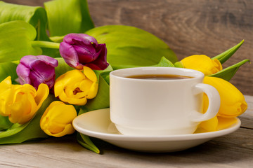 Yellow and purple tulips and coffee cup on rustic wooden table. Close up shot.