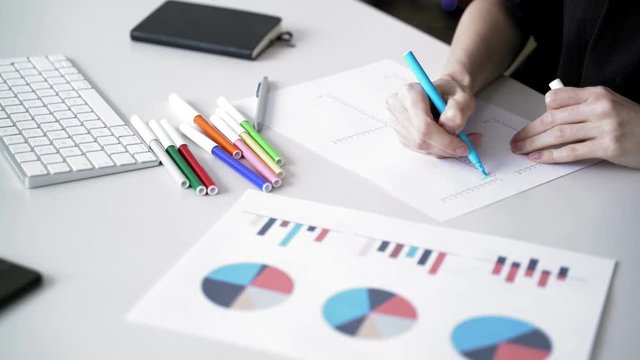 Woman fills data in graphs on paper. Records information. Woman is engaged in office work. Graphic charts,indicators. Woman works at the offside table. Woman draws symbols on the paper