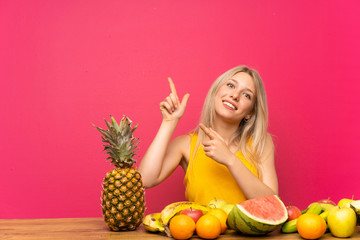 Young blonde woman with lots of fruits pointing with the index finger a great idea