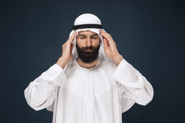 Half-length portrait of arabian saudi businessman on dark blue studio background. Young male model...