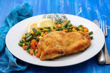fried chicken with boiled vegetables and lemon on white dish