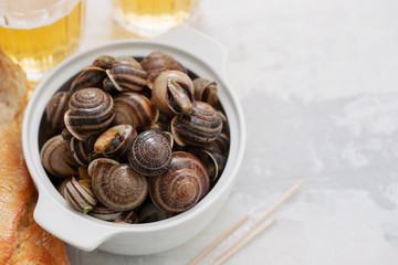 boiled snails with herbs in white bowl on ceramic background