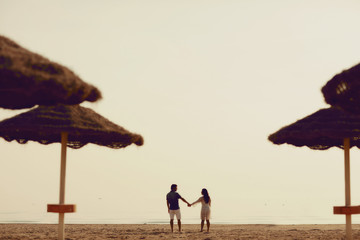 Couple in love having romantic tender moments on the beach near wicker umbrellas. Young lovers enjoying summer vacation