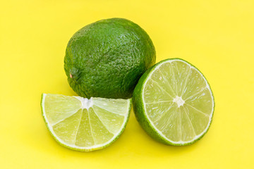 Lime on yellow background. Whole and half with slice of fresh green limes. citrus fruits