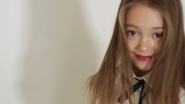A cute teen girl in a white blouse with a black tie and long hair posing in the Studio on a white background, she straightens her hair with her hands. Slow motion.