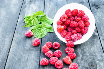 Fresh raspberry with leaves on the background of old dark boards. Selective focus.