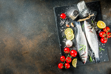Raw sea bass fish with spices and ingredients, ready for cooking, dark concrete background copy...