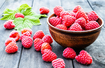 Ripe red raspberries on a bowl on the background of the old dark boards. Selective focus.