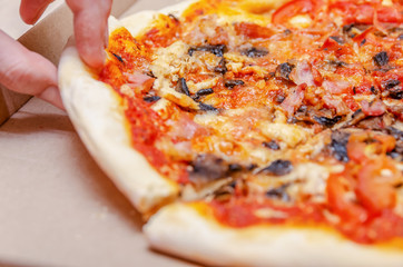 Female hand takes a piece of pizza from the box on the kitchen table close up