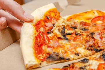 Female hand takes meat pizza with mushrooms from a simple cardboard box close up