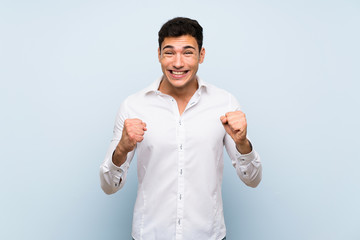 Handsome man over blue wall celebrating a victory in winner position