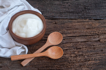 Natural homemade plain organic yogurt in wooden bowl and wood spoon on wood texture background